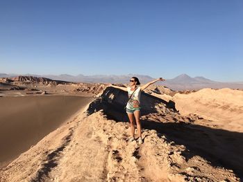 Woman with arms outstretched standing at desert against clear sky