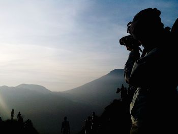 Silhouette people photographing on mountain against sky