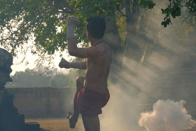 Side view of shirtless man standing exercising outdoors