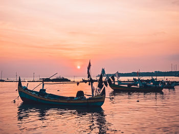 Boats moored in sea against sky during sunset