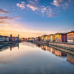 Bridge over river by buildings in city against sky during sunset