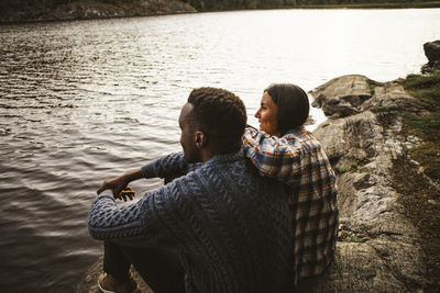 Side view of man and woman sitting by lake in forest