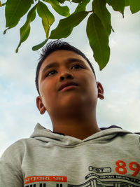 Low angle portrait of boy looking at camera against sky