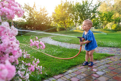 Full length of boy watering flowers in garden hose