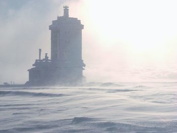 Lighthouse by sea against sky during sunset