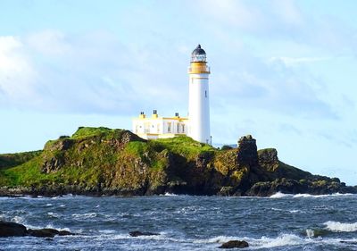 Lighthouse by sea against buildings and sky