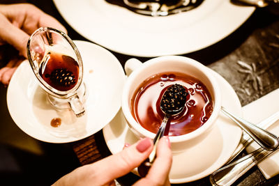 Cropped hands of woman holding pine cone jam over tea cup