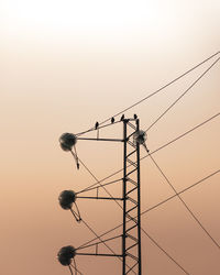 Low angle view of electricity pylon against clear sky during sunset