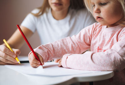 Midsection of girl drawing on book at table