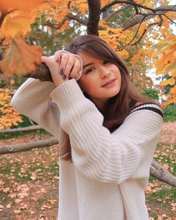 Portrait of young woman standing by tree during autumn