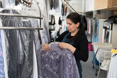 Mature female dry cleaner holding cleaned shirt in plastic while standing at laundromat