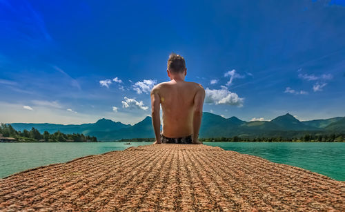 Rear view of shirtless man looking at mountains against sky