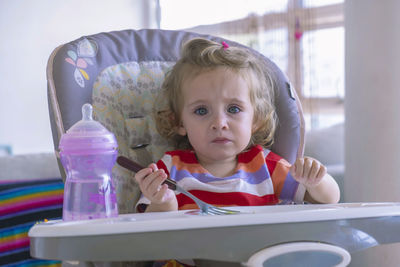 Little girl feeding alone in her chair in her living room.