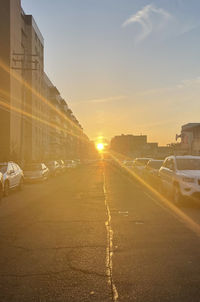 Road amidst buildings in city against sky during sunset