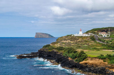 Lighthouse amidst sea and buildings against sky