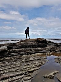 Full length of man standing on rock at beach against sky