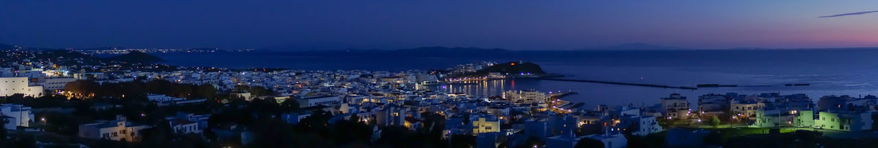 High angle view of illuminated buildings by sea against sky at dusk