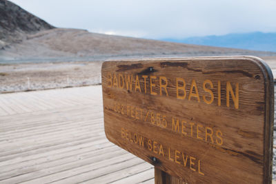 Close-up of text on wood at beach against sky