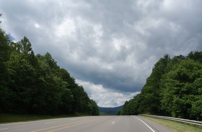 Empty road along trees and against sky