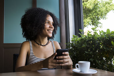 Young woman with smartphone sitting in a coffee shop looking out of window