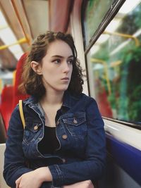 Young woman looking away while sitting on window