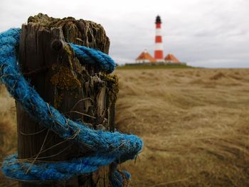 Close-up of rope on tree stump with lighthouse in background against cloudy sky