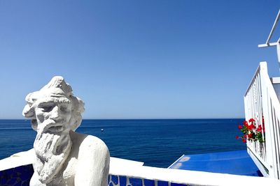 Statue by sea against clear blue sky