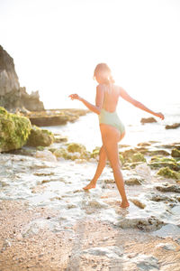 Rear view of young woman standing on beach against sky