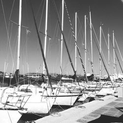 Row of sailboats moored by jetty in harbor against sky