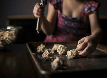 Midsection of girl placing batter on baking sheet at home