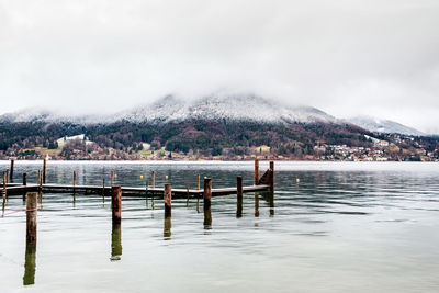 Wooden posts in lake against snowcapped mountains against sky