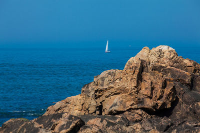 Rock formation in sea against clear blue sky