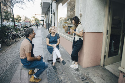 Male and female upholstery workers talking at sidewalk outside workshop