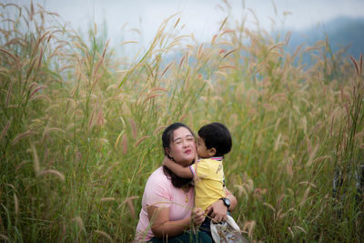 Son kissing mother while standing amidst plants