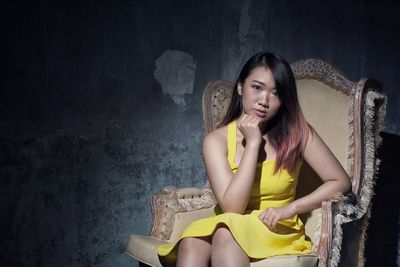 Portrait of young woman sitting on chair against wall