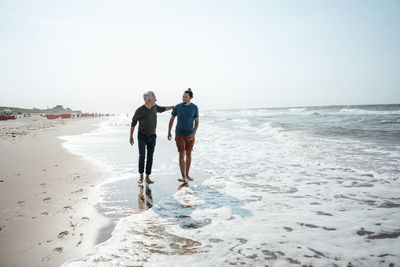 Rear view of man walking at beach against clear sky
