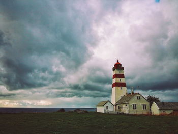 Houses and lighthouse on shore against cloudy sky