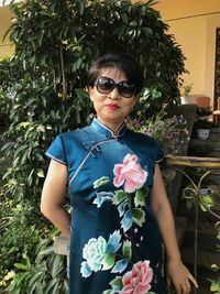 Portrait of smiling woman wearing sunglasses while standing against plants