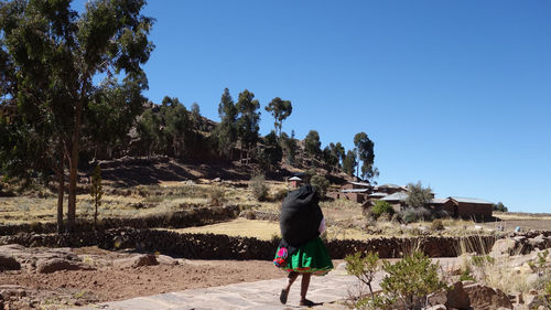 Rear view of woman walking on street against clear blue sky