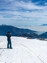 Full length of man standing on snowcapped mountain against sky