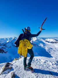 Rear view of man skiing on snowcapped mountain against clear blue sky