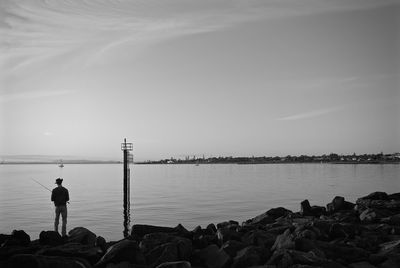 Rear view of man standing on rock and fishing at lake