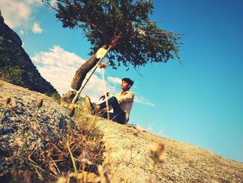 Man sitting on rock against sky