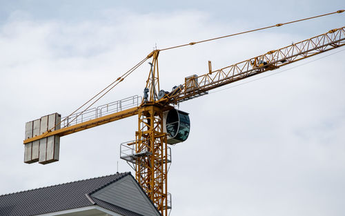 The high tower crane is working over the building in the construction site near the urban area.