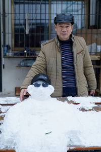 Portrait of man standing by snowman on bench