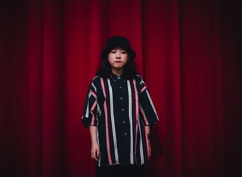 Portrait of woman standing against red curtain