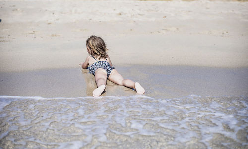 Back view of a 4 year old girl stretched on the beach.