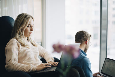 Young businesswoman sitting on chair using laptop by businessman at office cafeteria