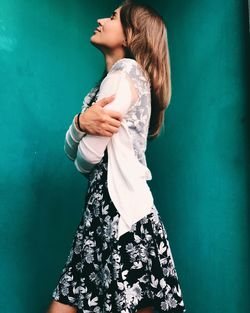 Side view of smiling young woman standing against wall