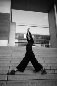 Full length portrait of woman exercising while standing on staircase against sky